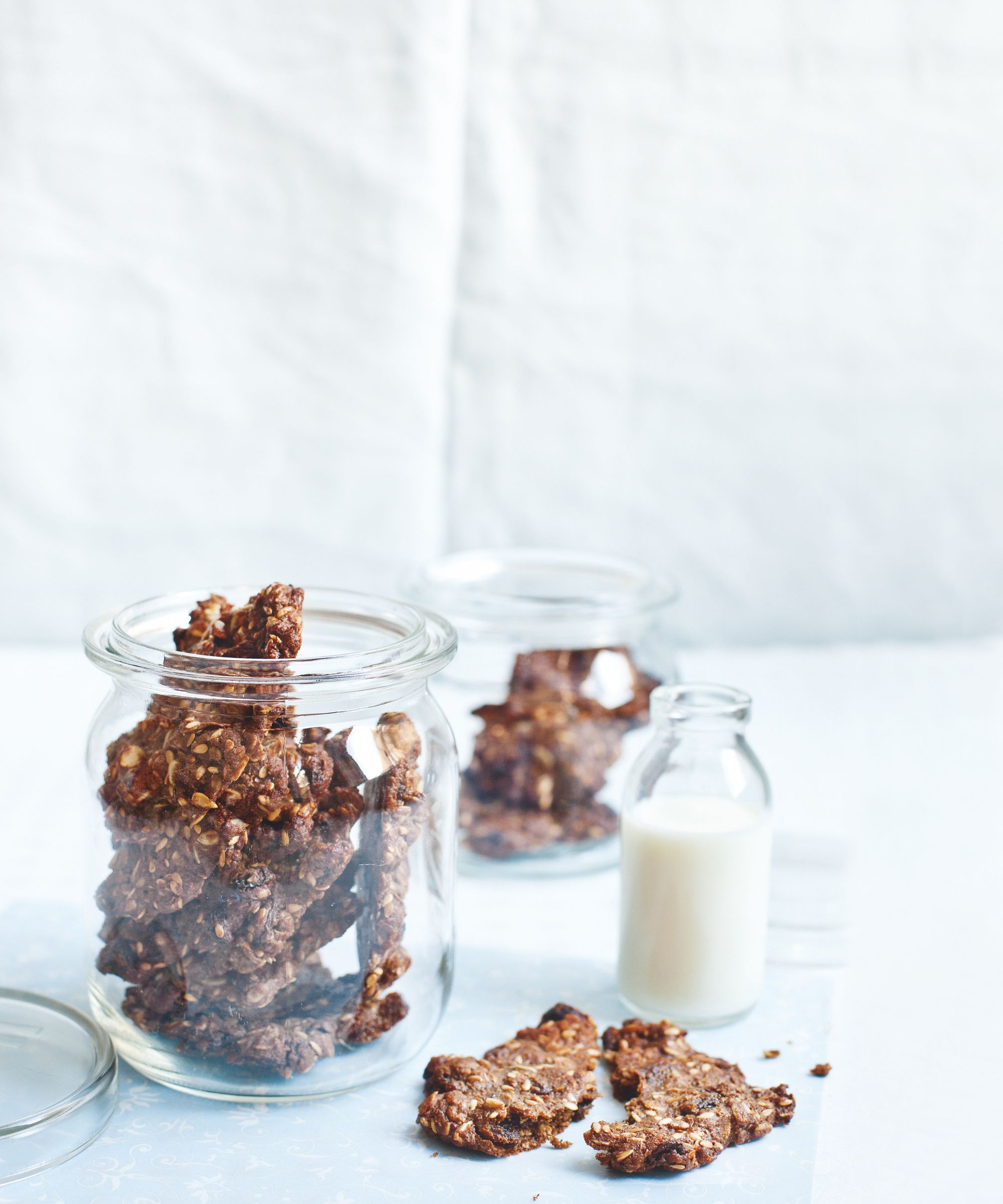 Two large mason jars filled with pieces of nut brittle, sitting on a white tablecloth alongside a small glass bottle of milk