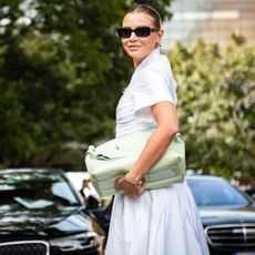 a guest at milan spring 2025 fashion week wearing white, dress mint bag, black sunglasses 