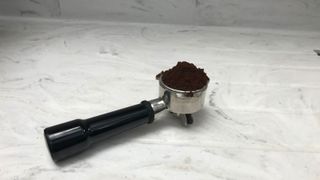 Breville The Barista Express' portafilter full of grounds on a marble countertop
