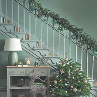 Mint green-painted hallway decorated for Christmas with a small Christmas tree and a garland covering the stair bannister