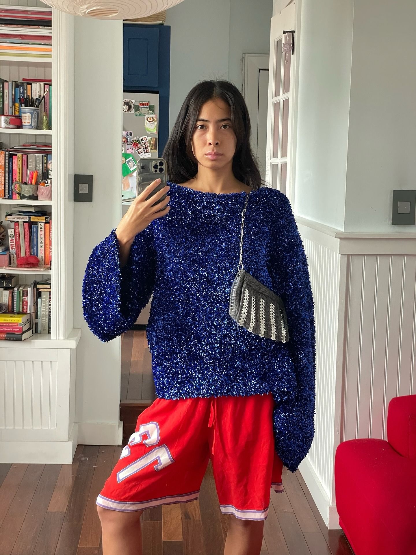 Woman wearing blue sweater, red board shorts, and striped bag.