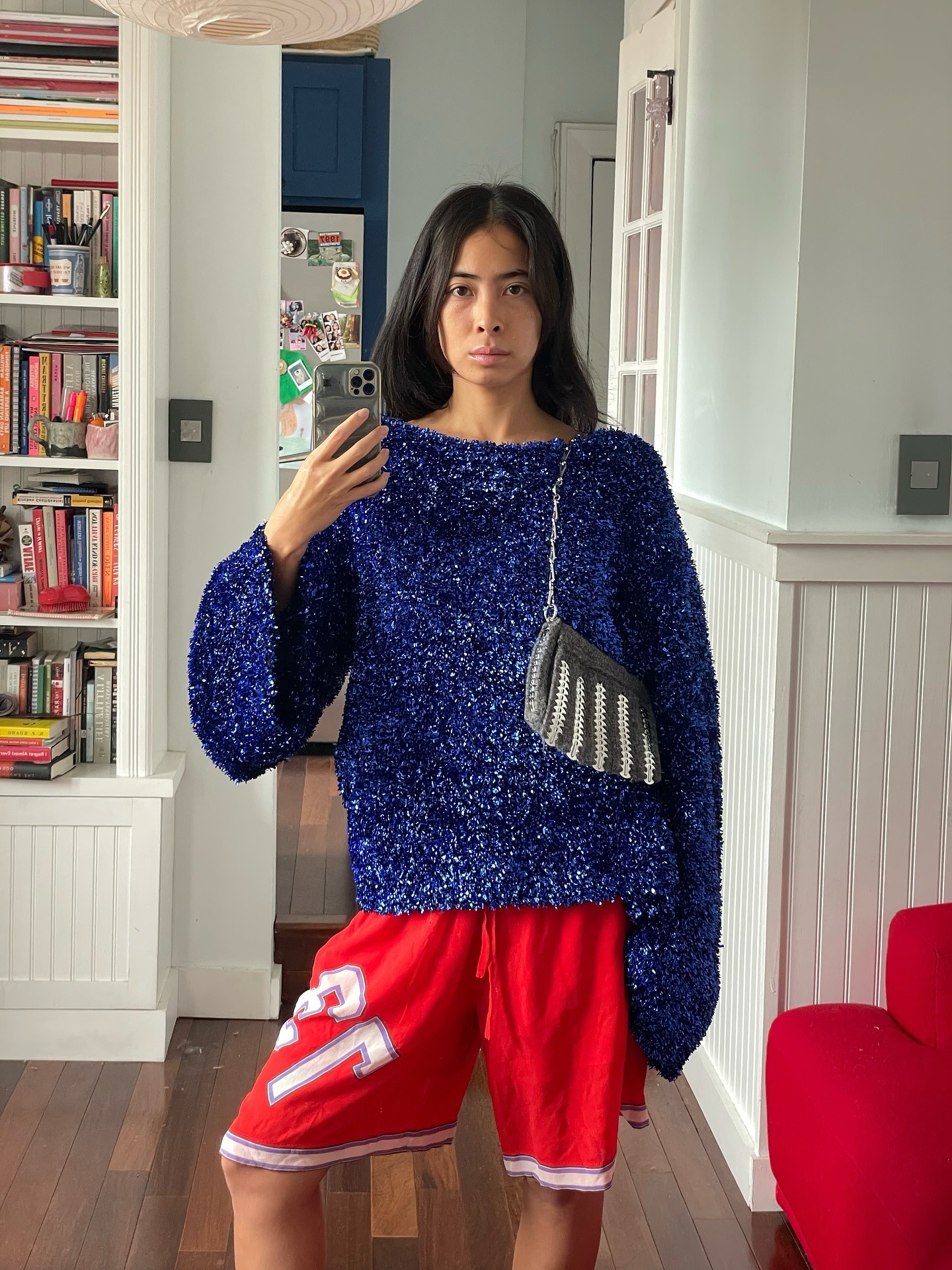 Woman wearing blue sweater, red board shorts, and striped bag.