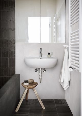 modern bathroom with black shower, black tiled floor, wooden rustic stool, white walls