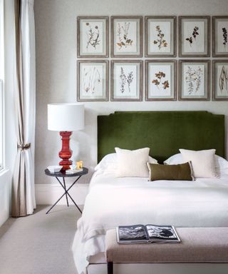 Master bedroom with bed with green headboard, white linen and cushions, green accent cushion, red table lamp on black bedside table, pressed flowers in frames above bed