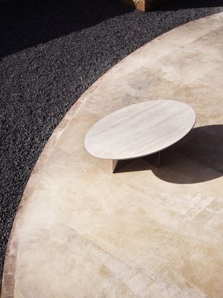 An oval coffee table with a travertine top and mirrored base