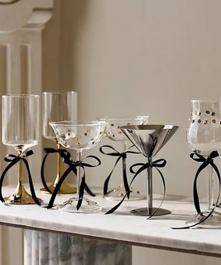 a marble table with various glassware including a stainless steel coupe all tied with black satin ribbon bows on the stems