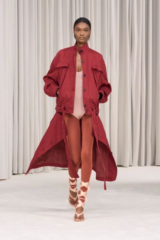 a Ferragamo model wears a leggings outfit of orange leggings, a pink bodysuit, red coat, and blush lace-up shoes.