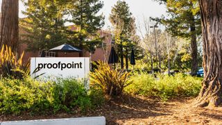 A white sign in the middle of a wooded area, partially obscured by bushes, with the word Proofpoint displayed