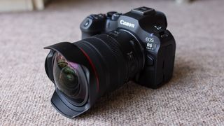 The Canon EOS R6 III with the Canon RF 7-14mm f/2.8-3.5L fisheye lens attached, on a brown carpet.