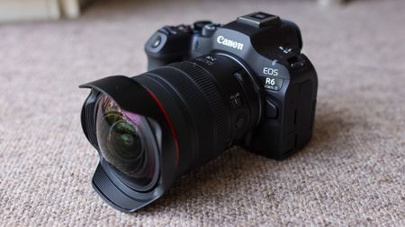 The Canon EOS R6 III with the Canon RF 7-14mm f/2.8-3.5L fisheye lens attached, on a brown carpet.