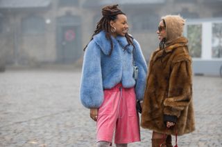 Two women stand at Copenhagen Fashion Week wearing a blue faux fur coat and a brown faux fur coat
