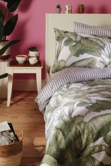 Primark home bedroom with pink walls, botanical leaf bed linen and a wooden side table with plant pots