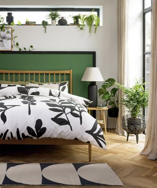 A green and white botanically inspired bedroom with leaf print duvet decor and assortment of indoor houseplants on shelf