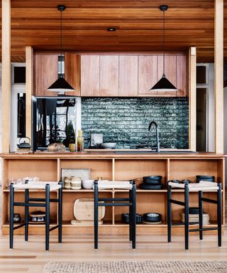 wooden kitchen with green tiled splashback, barstools and black pendant lights