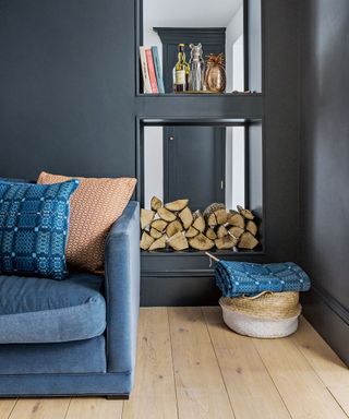 dark blue living room with blue sofa, chopped fire wood and basket