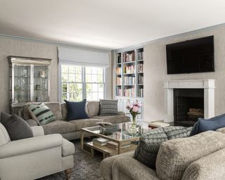 A neutral living room with grey sofas, white armchair and a large TV over the fireplace