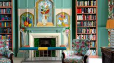 A large sitting room with bookshelves either side of a fireplace. The walls are painted in a bright light teal color, an the fireplace has a handpainted mural in a Bloomsbury style.