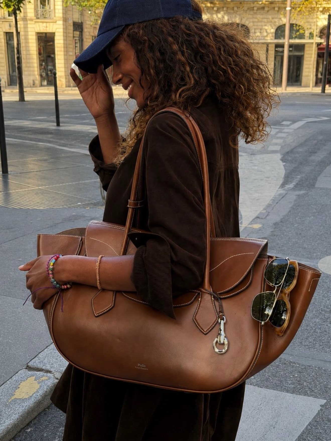 An image of an influencer in Paris wearing a navy baseball cap and chocolate brown velvet shirt carrying a large brown leather handbag tote