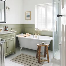 White painted bathroom with green wall panelling, a freestanding bath with a wooden stool next to it