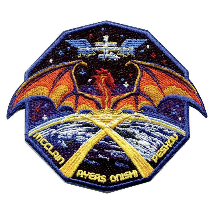 an embroidered 10-sided patch depicting a space station, a mythological dragon and Earth, the latter with criss-criossing contrails forming the roman numeral 