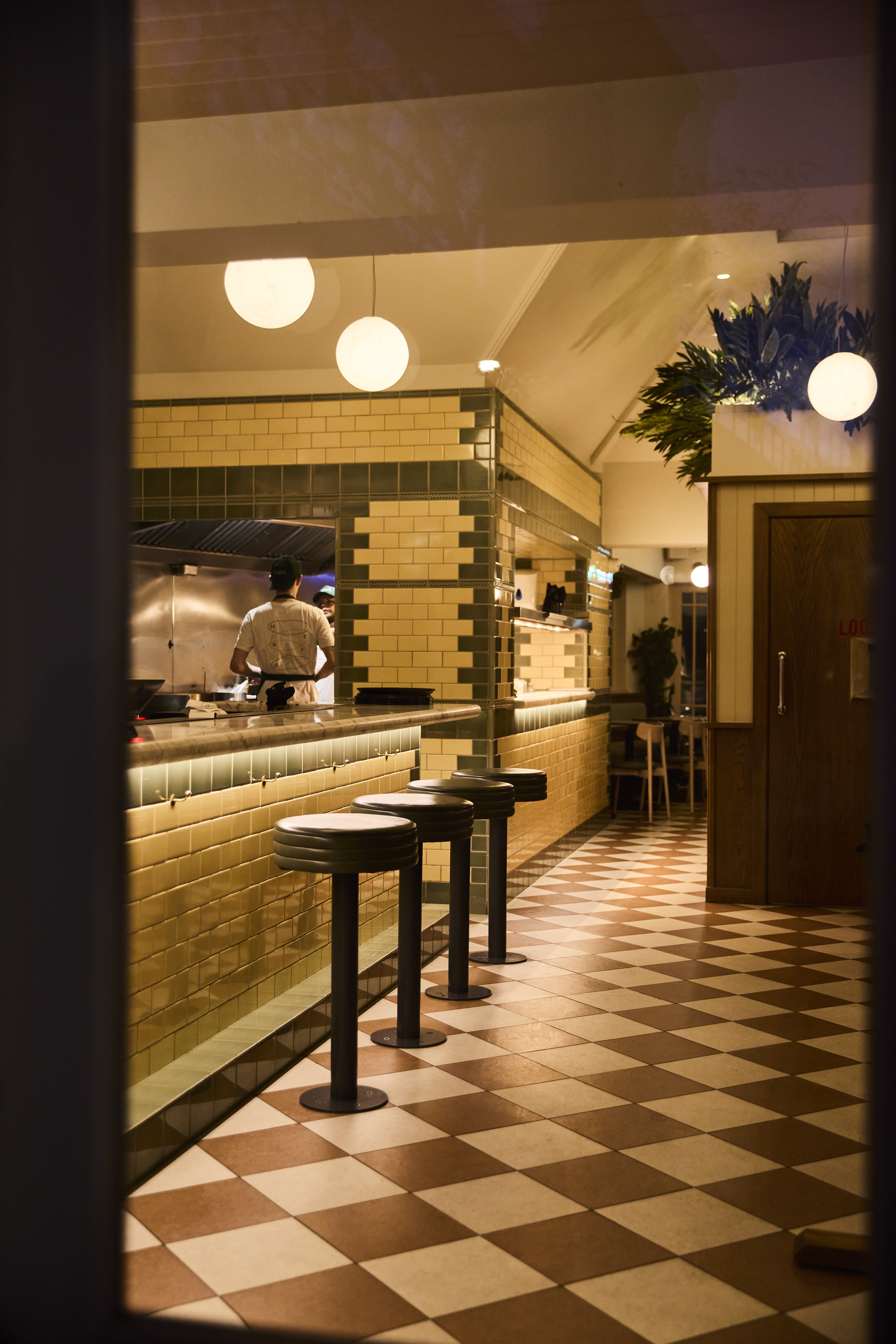 A chic burger restaurant with tiled floors, spherical art deco lighting, and ochre and green tiling.