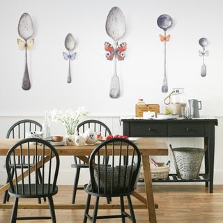 White dining room with wood table and chairs painted black. Oversized spoons mural on the wall.