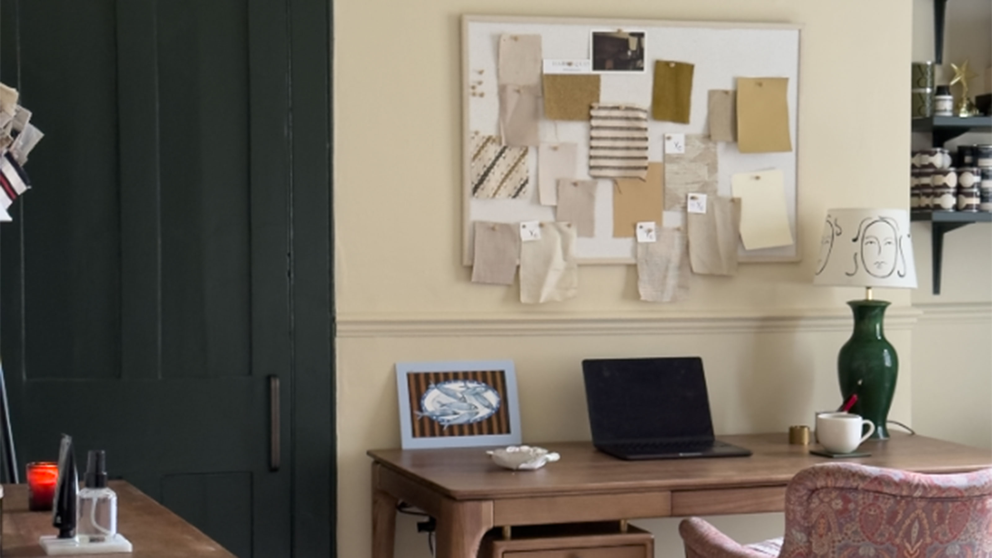 Neutral home office with wooden desk, patterned upholstered armchair and pinboard on wall above desk showing fabric samples