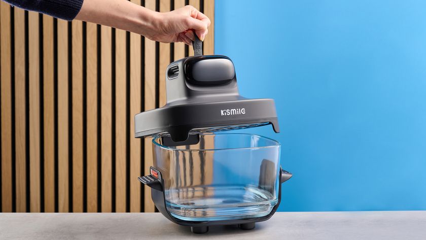 the kismile roasti air fryer with a glass cooking container photographed against a blue and wood background, showing the heating element lid