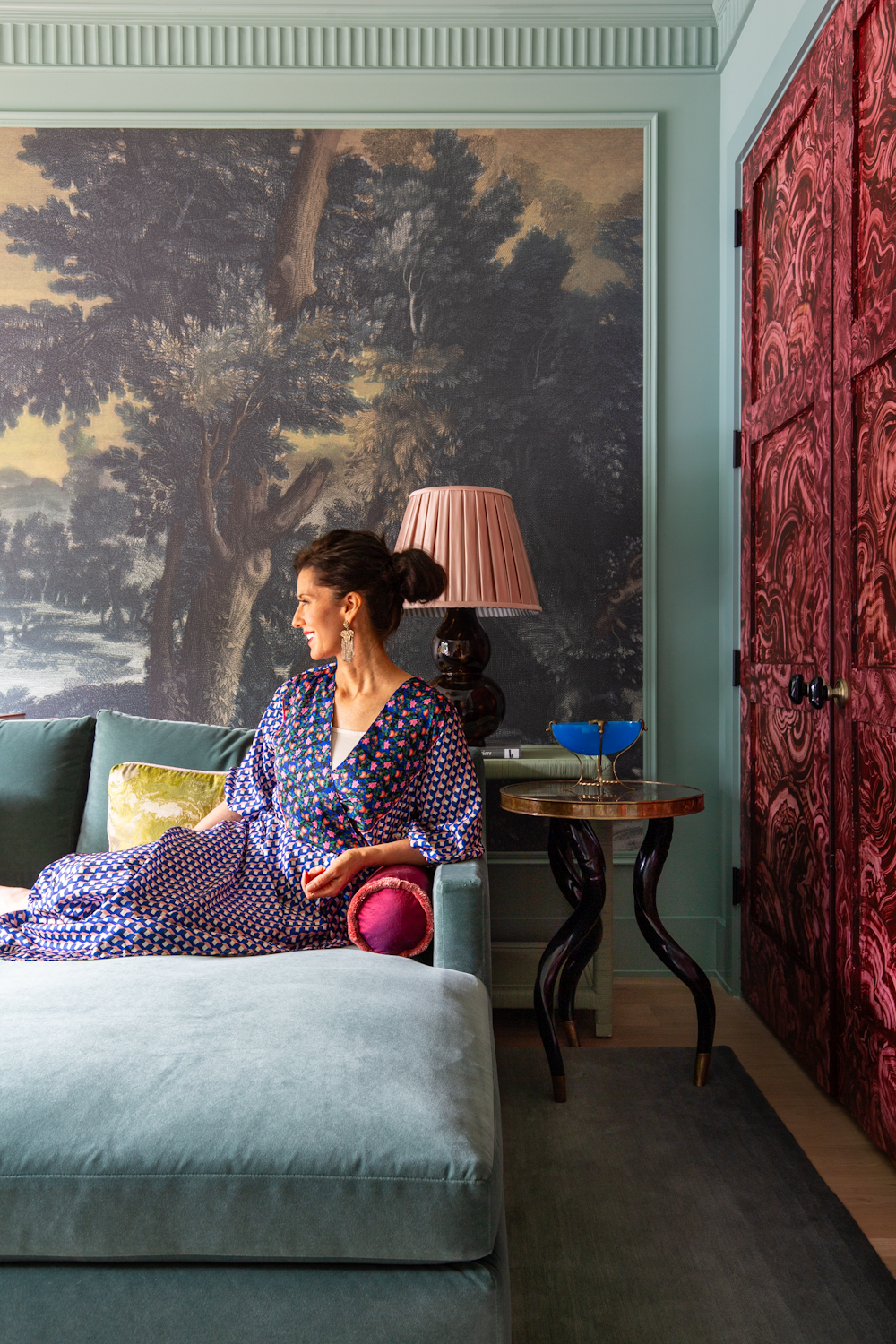 A living room with a botanical wallcovering, imitation &#039;jewel&#039; doors, and a woman sat on a blue sofa
