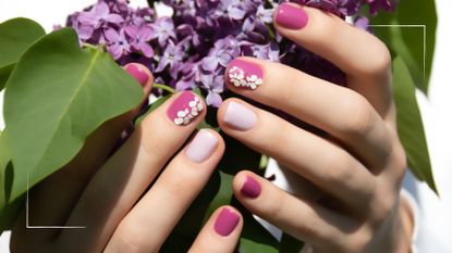 A hand with a floral spring nail design holding purple flowers