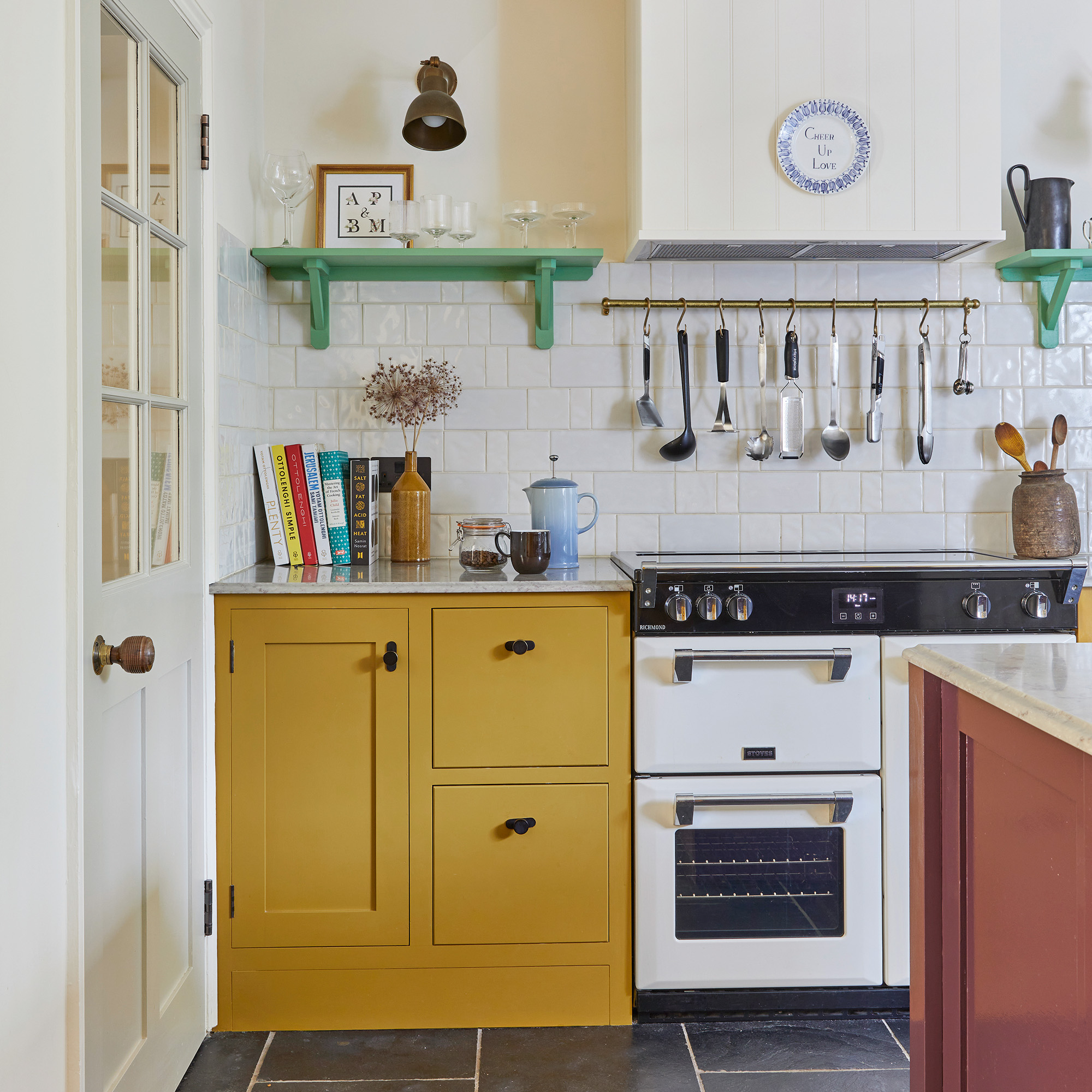 kitchen with yellow cabinetry and white range cooker style over, green open shelves and plum-coloured island