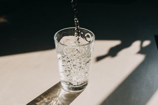 Cancer care: Water being poured in a glass of water that cast a beautiful shadow on a white kitchen countertop