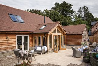The exterior of an oak frame home with larch cladding and a patio area with festoon lights and garden furniture