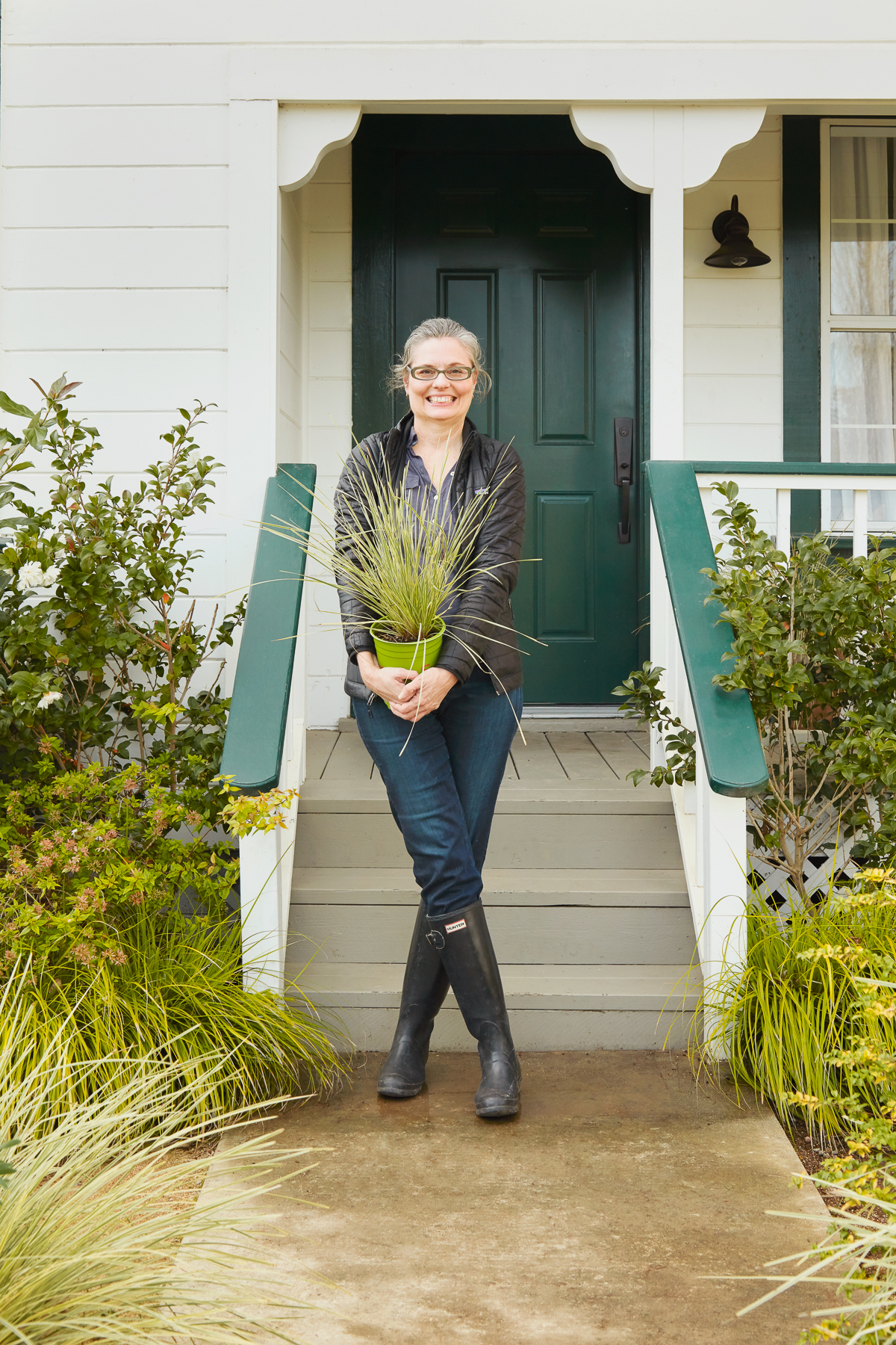 Janet Sluis holding a plant in front of a porch