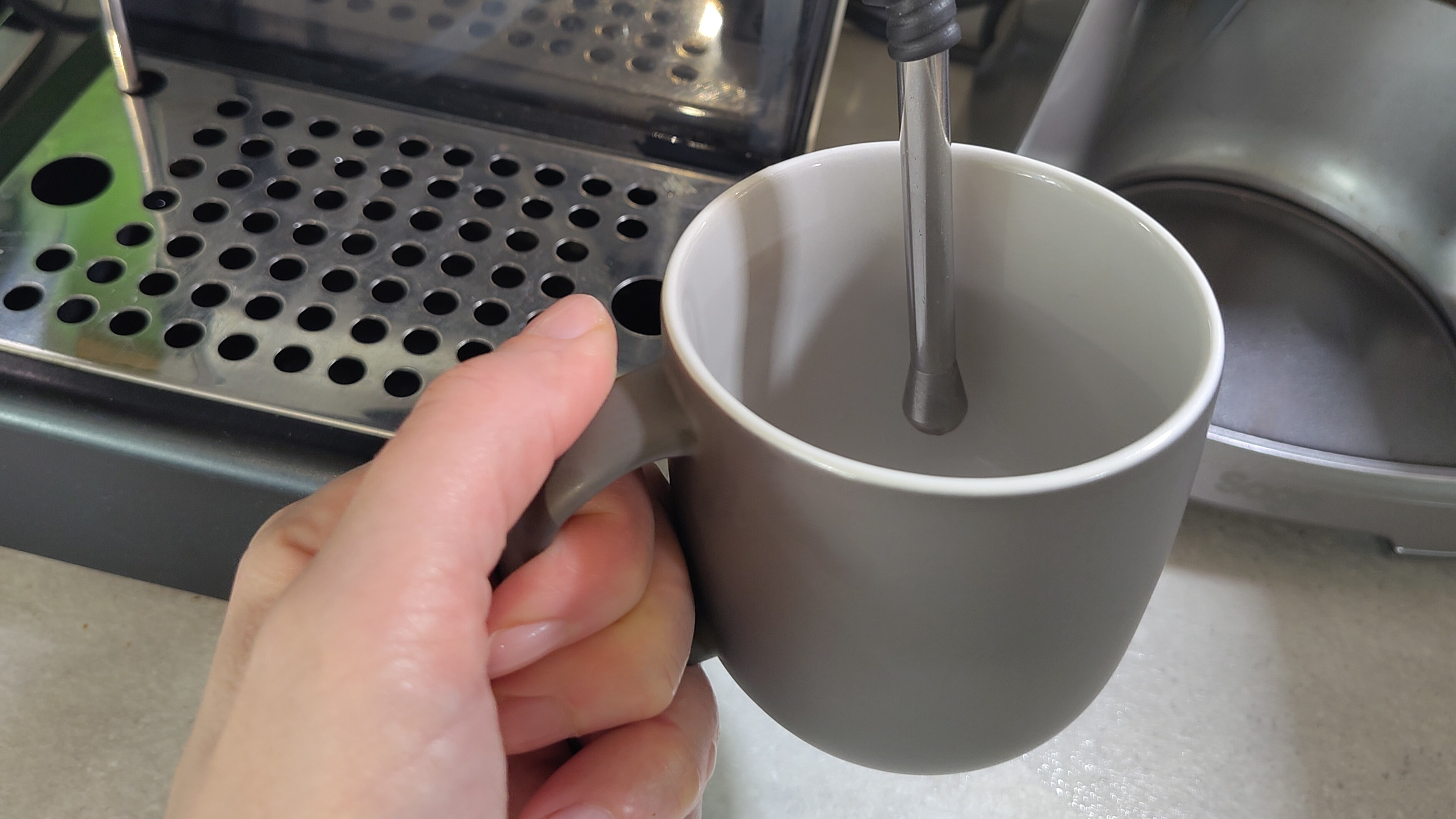 Person heating cup using coffee maker steam wand