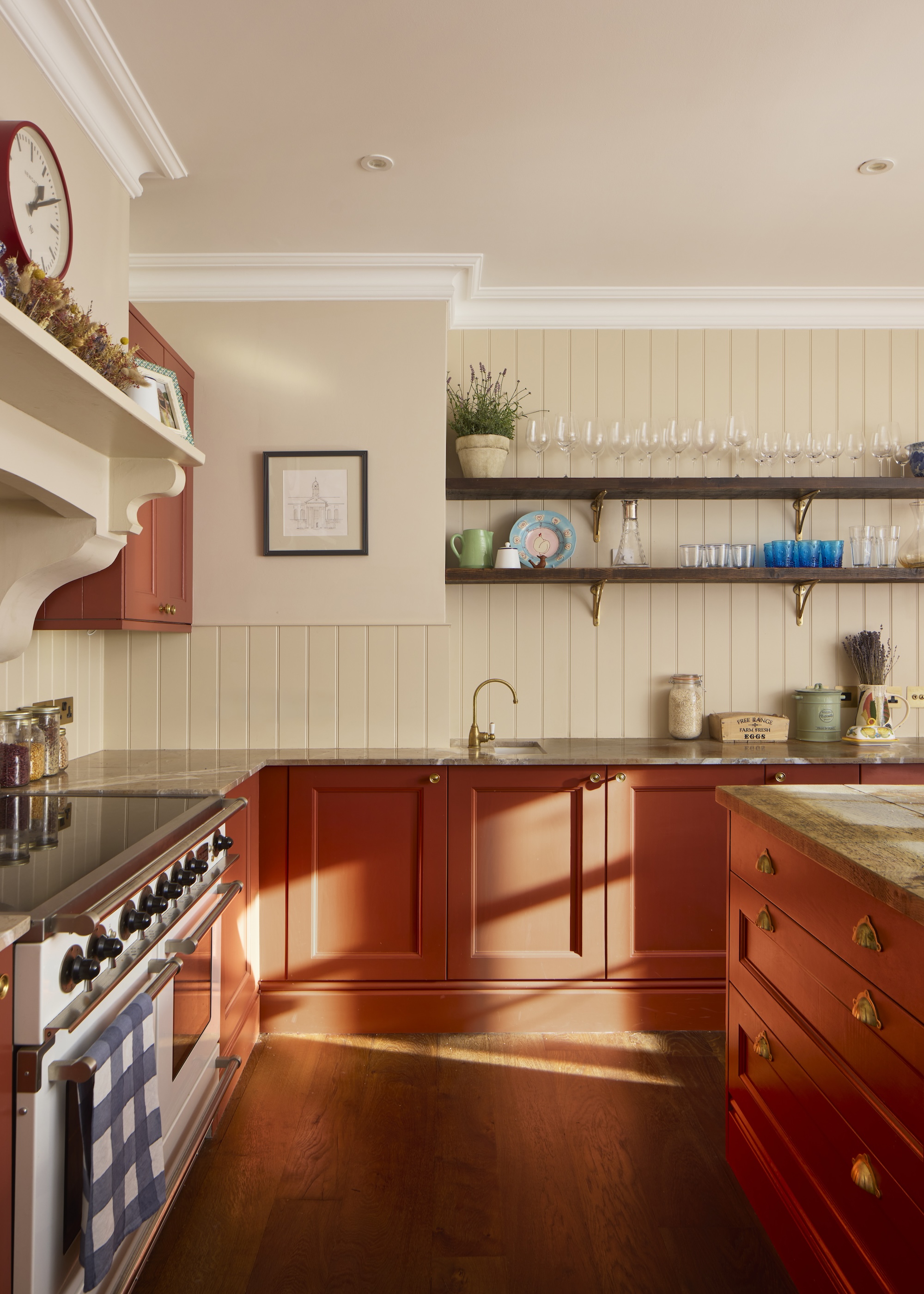 A small kitchen with red/orange cabinets as well as open shelving above the cabinets that is holding lots of glassware