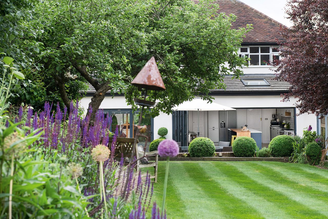 garden with colourful plants, bushes and open bifold doors leading into an open-plan kitchen diner 