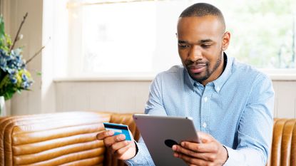 A man holds a credit card in one hand while he looks at a tablet in the other.