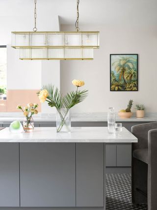 white and grey kitchen with gold chandelier, tiled floor, artwork