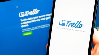 Hand holding a phone that says Trello with same welcome page on laptop in background