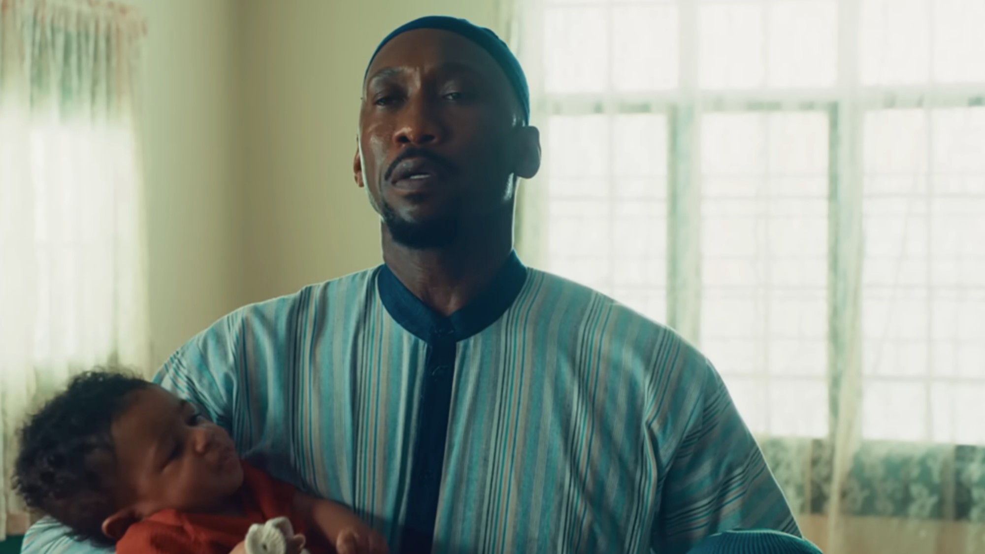 Mahershala Ali in traditional muslim clothing holding a baby in Your Mother Your Mother Your Mother