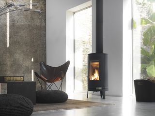 Fire in woodburning stove set in living room with large windows, white walls and a brown feature wall on the side