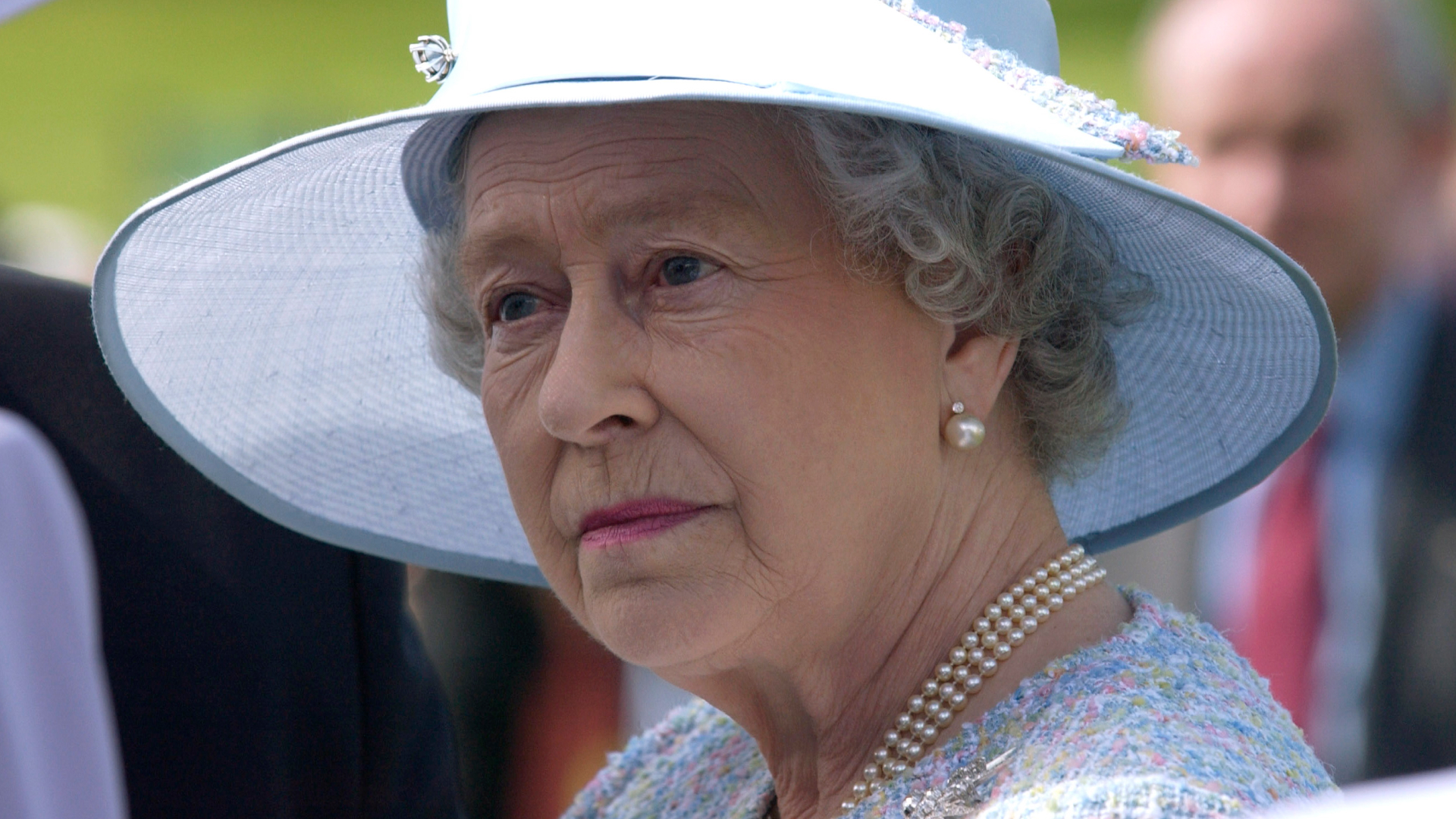 Queen Elizabeth wears a blue hat and a pearl necklace