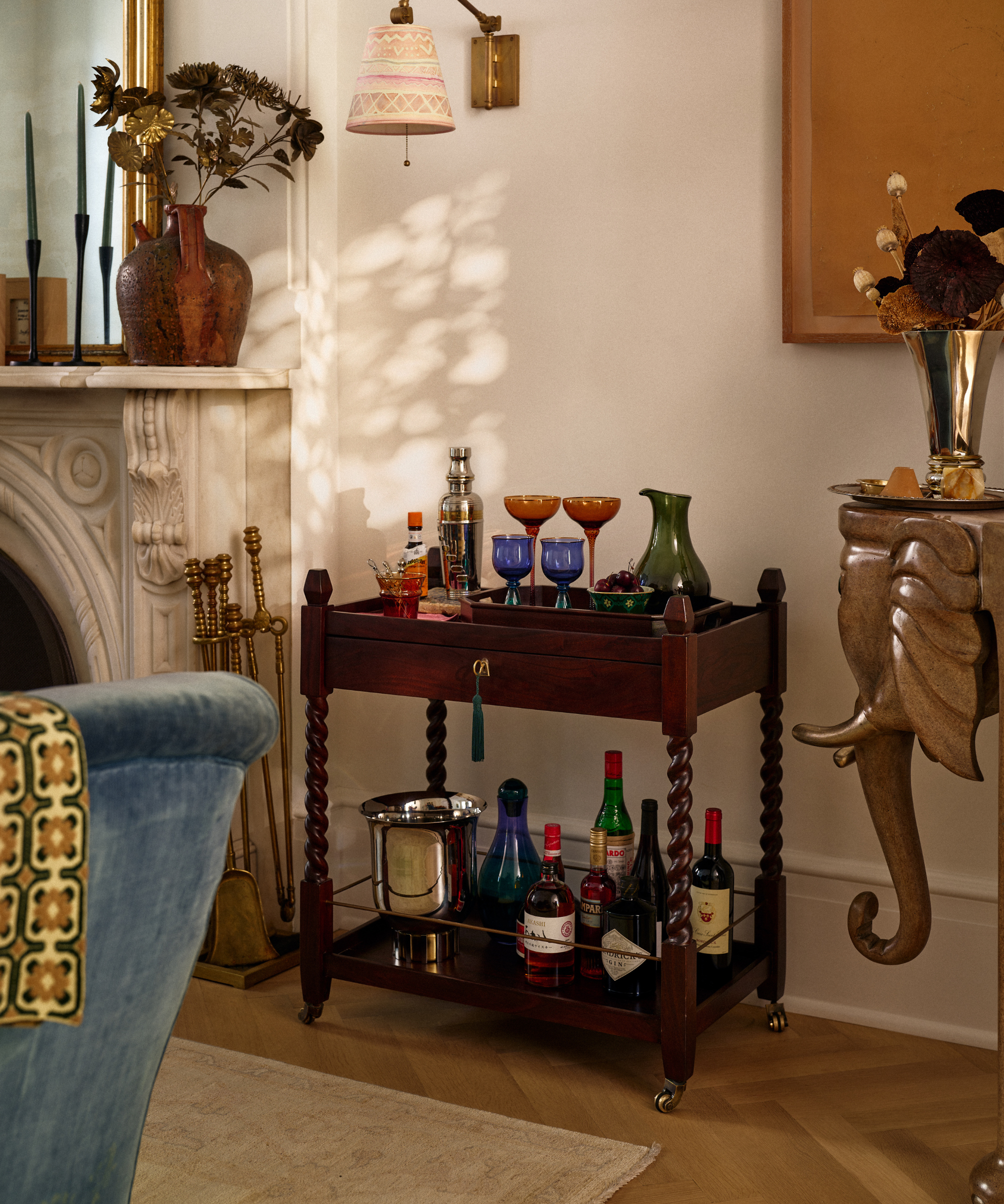 Jon Batiste and Suleika Jaouad x Anthropologie wooden bar cart holding coupe glasses, a champagne bucket, and bottles of liquor.