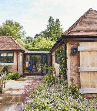 a glazed extension addition between two solid wall extensions - two brick homes joined by a glass walkway, with a person walking through it, and a garden