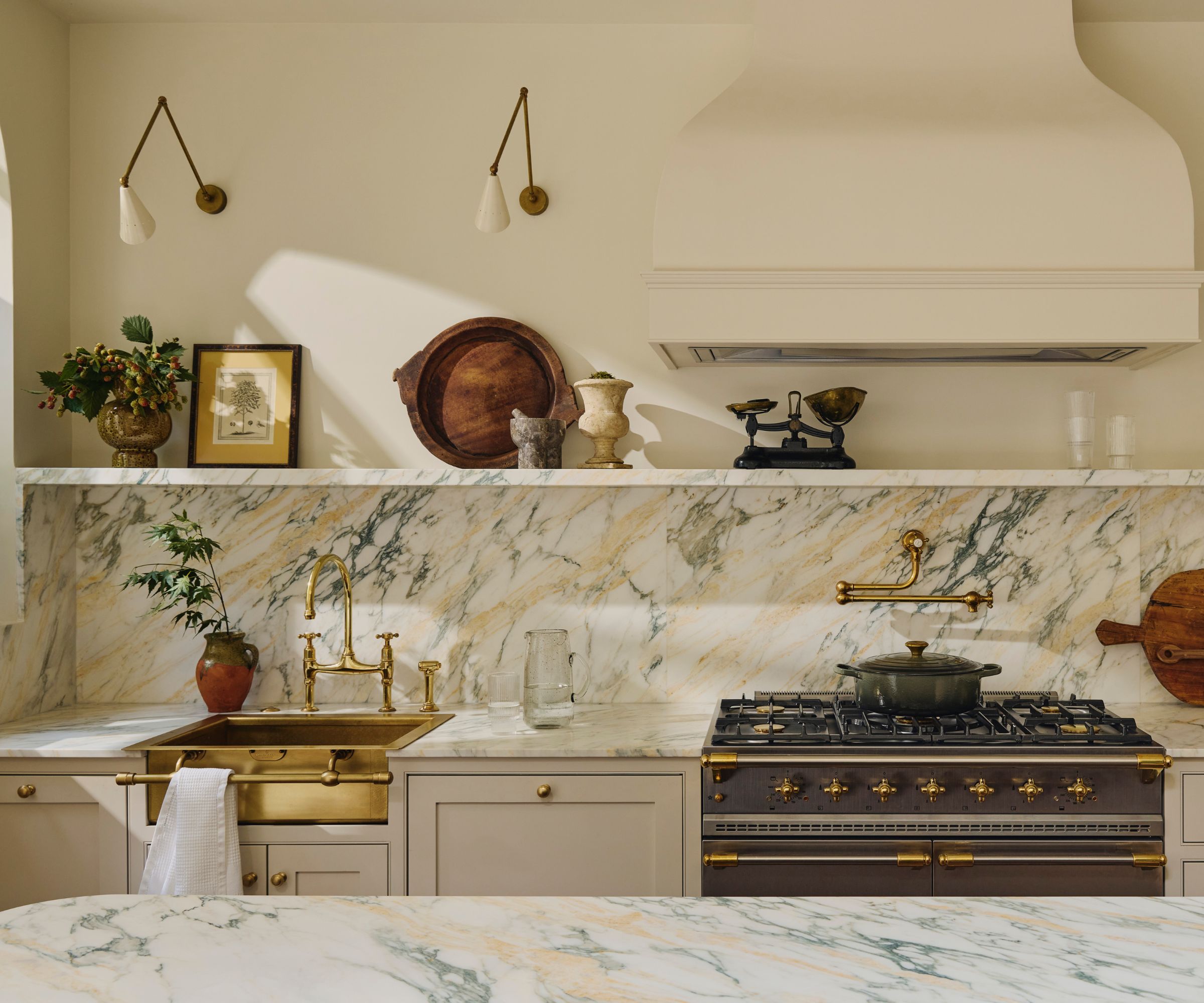 A neutral kitchen with Calcutta marble countertops and matching backsplash and a brass sink
