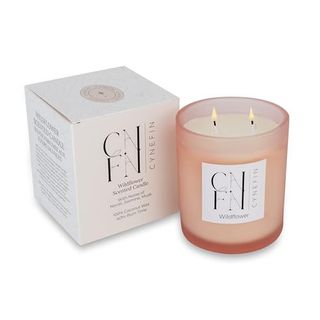 A pink glass candle jar with a lit two wick candle inside. A white cardboard box beside