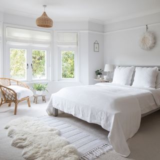 Main bedroom with white walls, white bedding and white faux sheepskin rug
