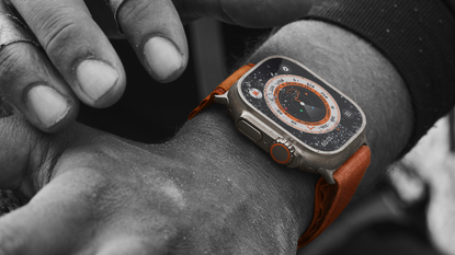 Apple Watch Ultra on man's wrist with orange strap and silver casing