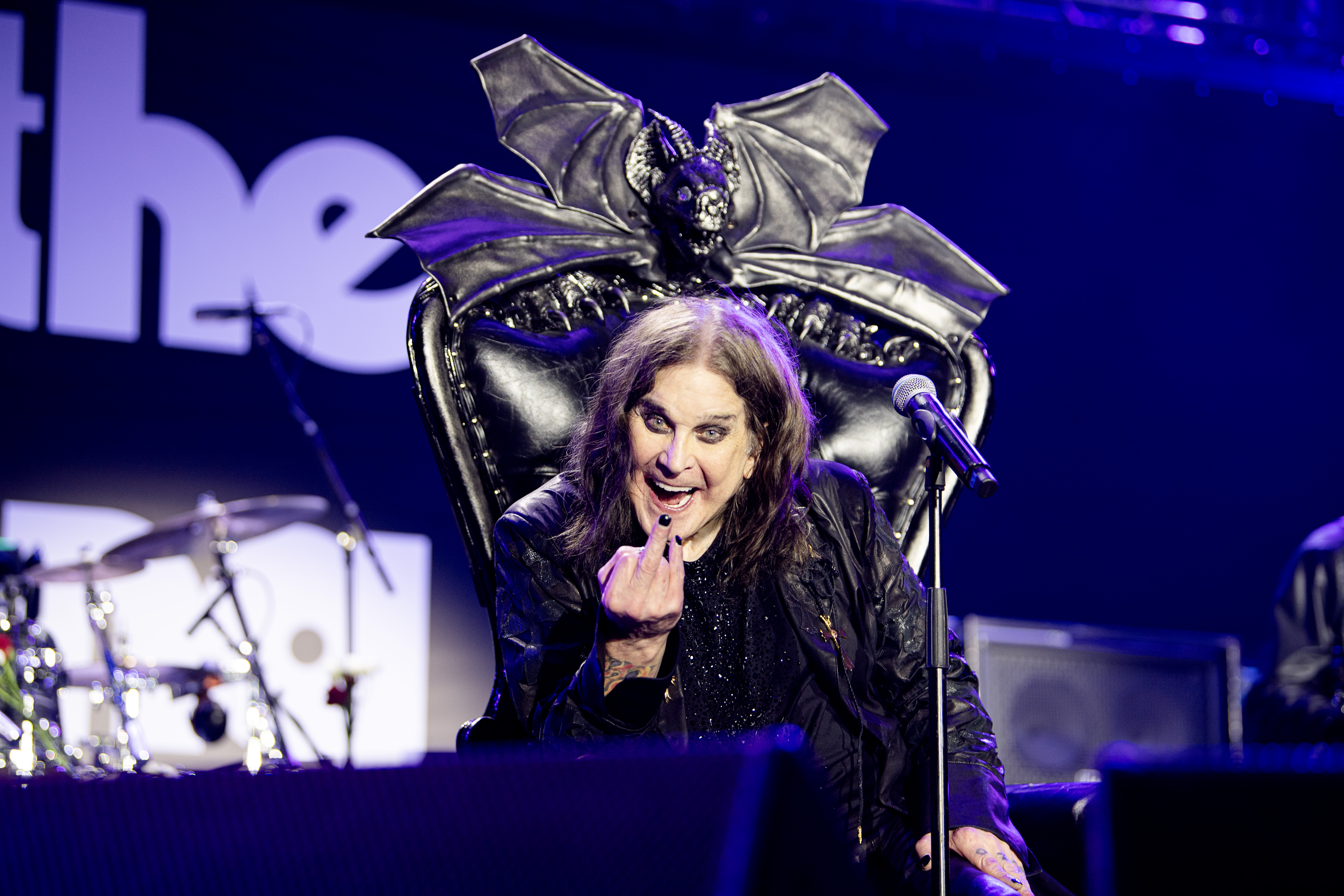 Ozzy Osbourne holding a finger up at the camera from his throne on stage